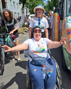 Zwei Frauen neben dem CSD Bus. Eine davon im Rollstuhl Text: Pfennigparade Die Zukunft zählt auf uns. Wir lieben euch alle. www.pfennigparade.de