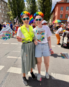 Zwei Frauen bunt verkleidet nebeneinander auf der Straße Text Wir lieben euch alle.